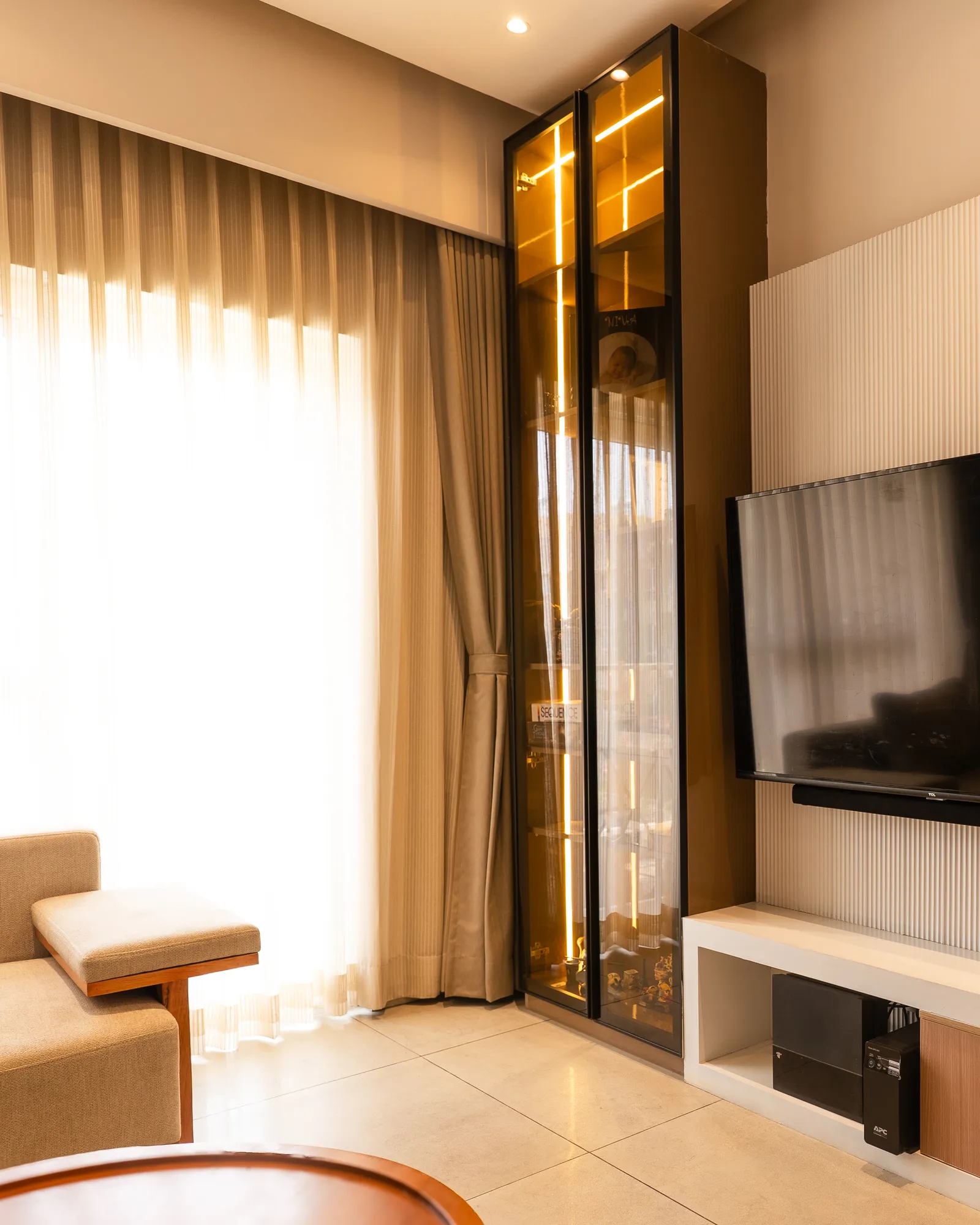 Lit glass-front display cabinet in the living room — Amlan's Residence